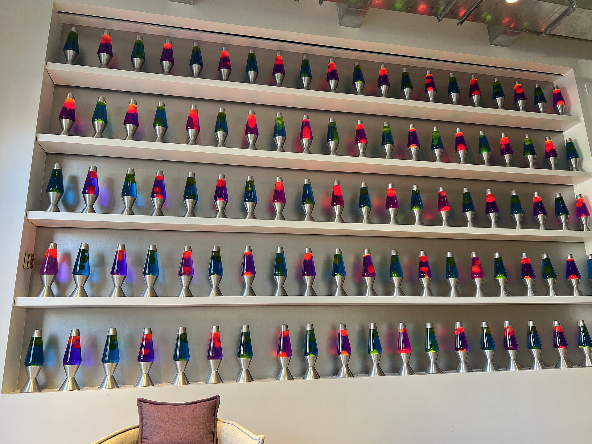 A wall of roughly 100 lava lamps with glowing wax blobs in various colors suspended in illuminated tubes, installed in the lobby of Cloudflare's San Francisco office. A camera pointed at the wall captures the unpredictable movement of the blobs to generate truly random numbers for encryption.
